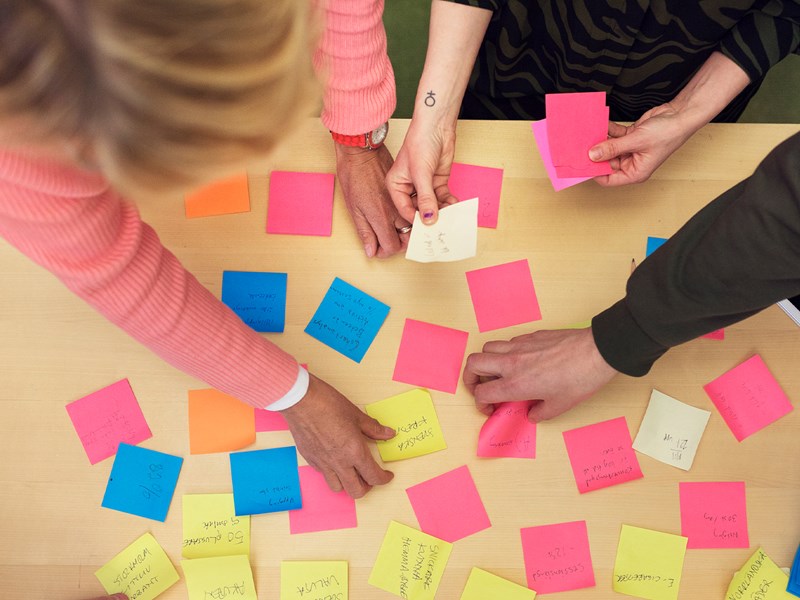 Händer runt post-it-lappar med anteckningar.